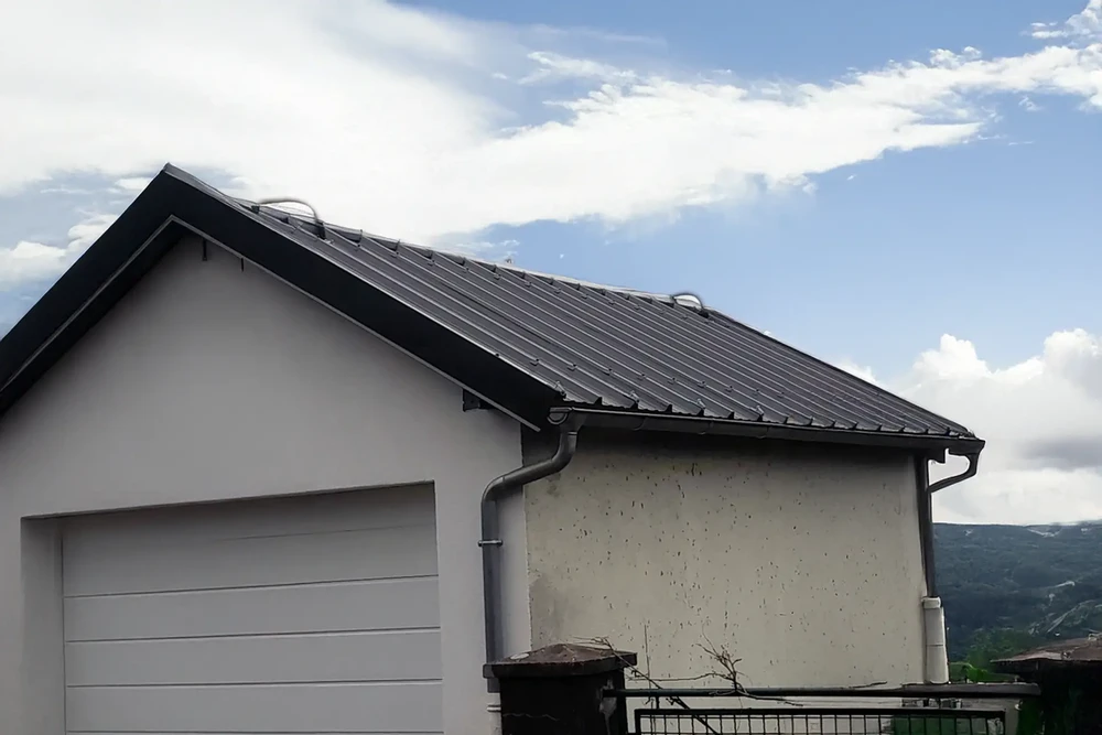 Maison individuelle avec toiture métallique en bac acier gris anthracite, gouttières PVC grises et descentes pluviales
