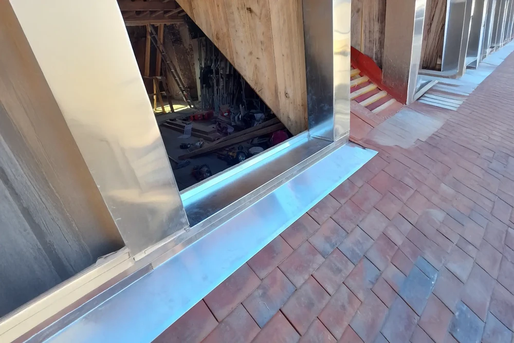 Cheminée en briques anciennes sur toiture résidentielle, extérieur jour ensoleillé, arbres en arrière-plan, ciel bleu dégagé