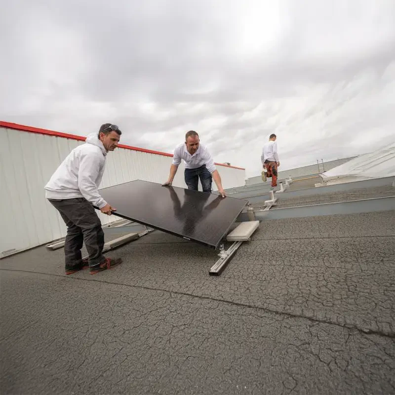 Ouvrier en tenue noire installant des panneaux photovoltaïques sur toiture résidentielle par temps ensoleillé